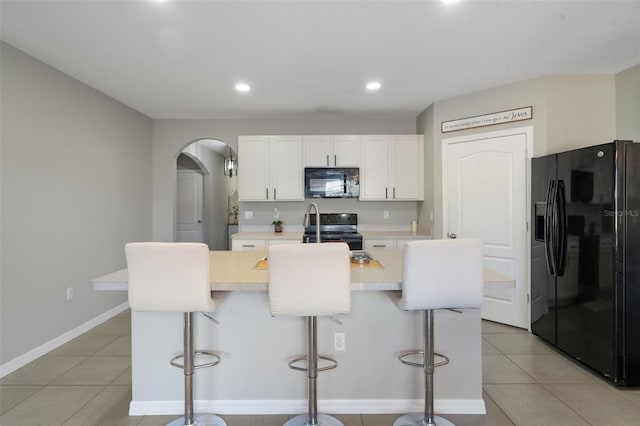 kitchen featuring white cabinetry, a kitchen island with sink, a breakfast bar area, and black appliances