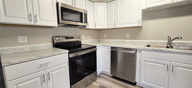 kitchen with light stone countertops, appliances with stainless steel finishes, sink, light hardwood / wood-style flooring, and white cabinets