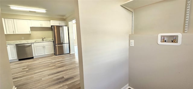 kitchen with appliances with stainless steel finishes, ornamental molding, sink, light hardwood / wood-style flooring, and white cabinets