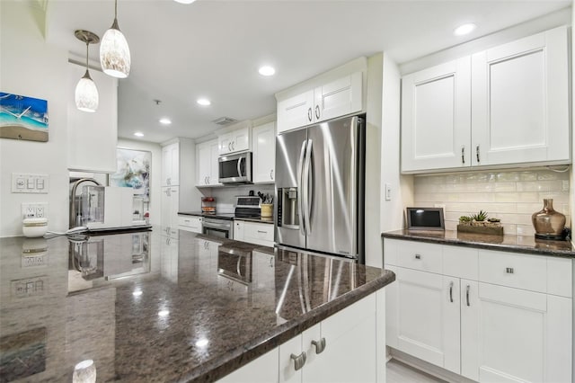 kitchen with appliances with stainless steel finishes, backsplash, dark stone counters, pendant lighting, and white cabinetry