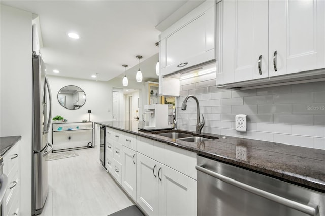 kitchen featuring decorative backsplash, white cabinets, appliances with stainless steel finishes, dark stone countertops, and a sink