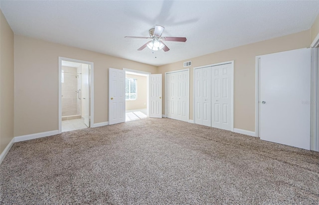 unfurnished bedroom with ceiling fan, light carpet, connected bathroom, and two closets