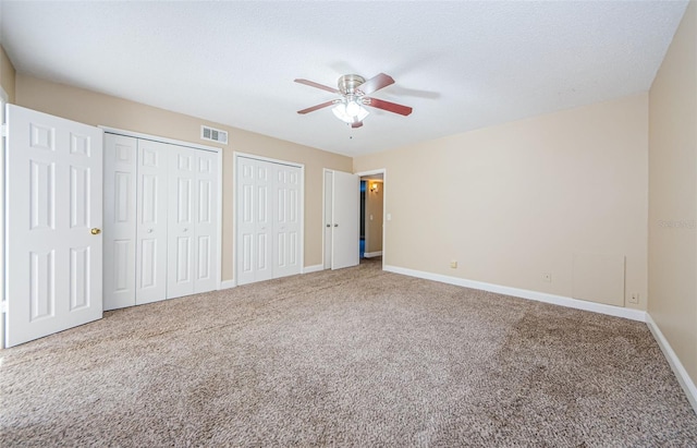 unfurnished bedroom featuring carpet flooring, ceiling fan, a textured ceiling, and two closets