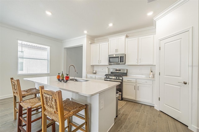 kitchen featuring appliances with stainless steel finishes, a breakfast bar, white cabinetry, an island with sink, and sink