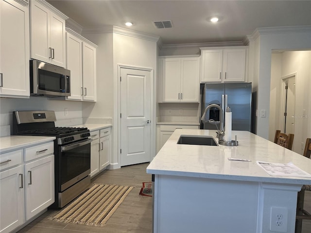 kitchen with stainless steel appliances, an island with sink, sink, and white cabinets