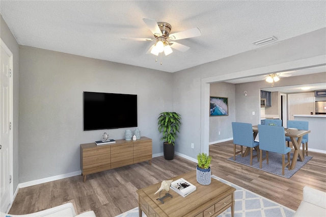 living room featuring hardwood / wood-style flooring, ceiling fan, and a textured ceiling