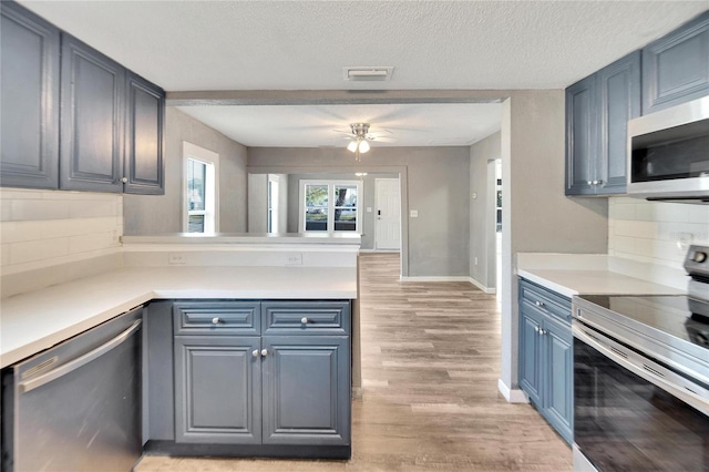 kitchen featuring ceiling fan, tasteful backsplash, light hardwood / wood-style floors, a textured ceiling, and appliances with stainless steel finishes