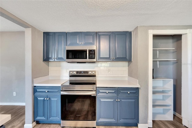 kitchen with tasteful backsplash, blue cabinets, light wood-type flooring, and appliances with stainless steel finishes