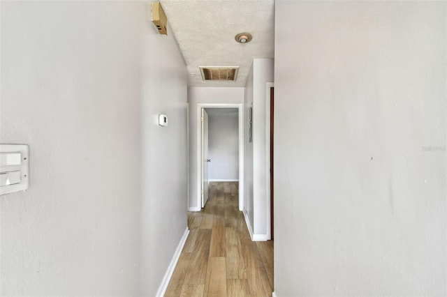 corridor with a textured ceiling and light hardwood / wood-style floors