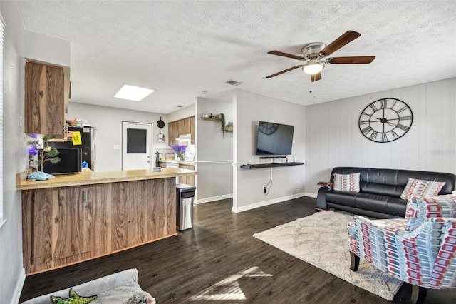 living room with a textured ceiling, dark wood-type flooring, wooden walls, and a skylight