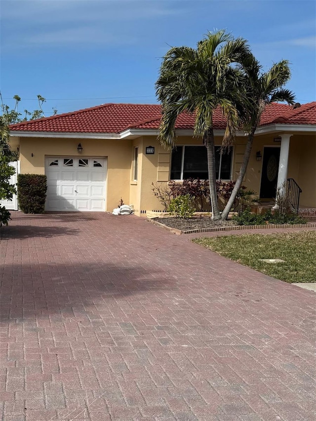 view of front of house with decorative driveway, a tile roof, an attached garage, and stucco siding