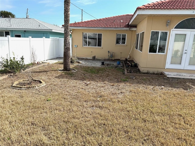 back of house featuring french doors, a tile roof, stucco siding, a lawn, and fence