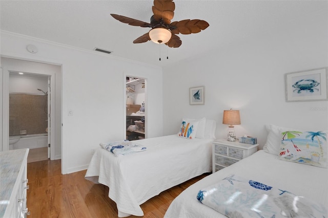 bedroom featuring a walk in closet, crown molding, ceiling fan, light hardwood / wood-style floors, and a closet