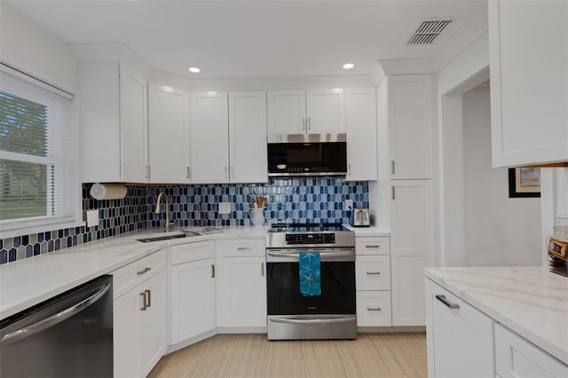 kitchen featuring sink, light stone counters, backsplash, white cabinets, and appliances with stainless steel finishes