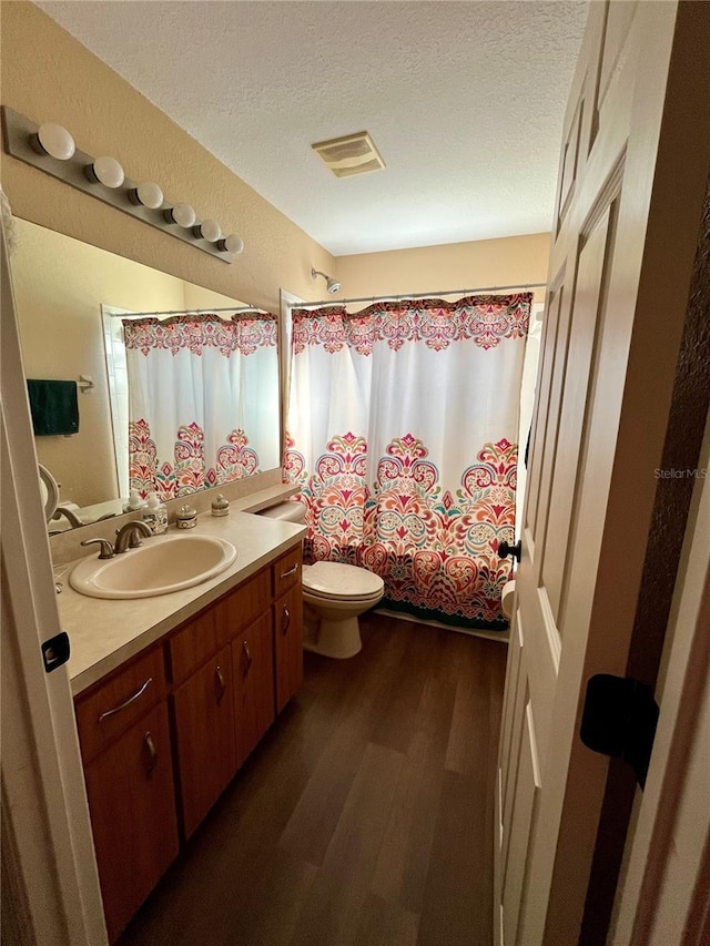 full bathroom featuring hardwood / wood-style floors, a textured ceiling, toilet, shower / tub combo with curtain, and vanity