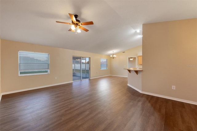 unfurnished living room featuring dark wood-type flooring, vaulted ceiling, baseboards, and ceiling fan with notable chandelier