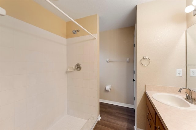 full bath featuring baseboards, tiled shower, wood finished floors, and vanity