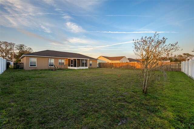 rear view of property featuring a fenced backyard, a lawn, and stucco siding