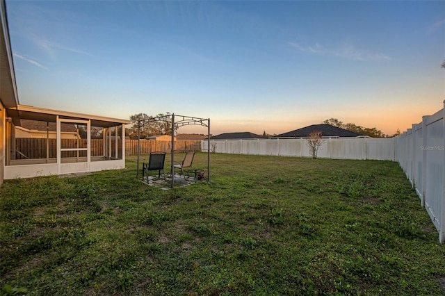 yard at dusk featuring a sunroom and a fenced backyard