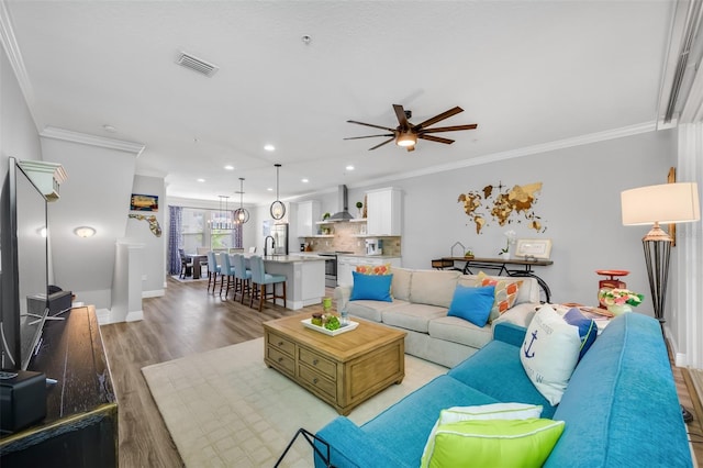 living room with crown molding, light hardwood / wood-style flooring, ceiling fan, and sink