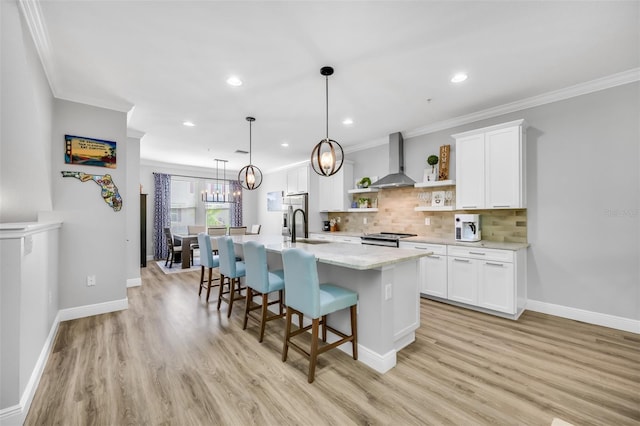 kitchen with white cabinets, wall chimney exhaust hood, light wood-type flooring, and a kitchen island with sink