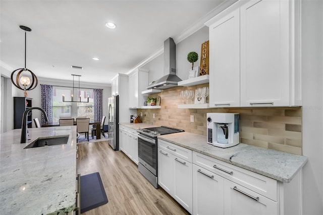 kitchen with sink, wall chimney exhaust hood, stainless steel appliances, decorative light fixtures, and white cabinets