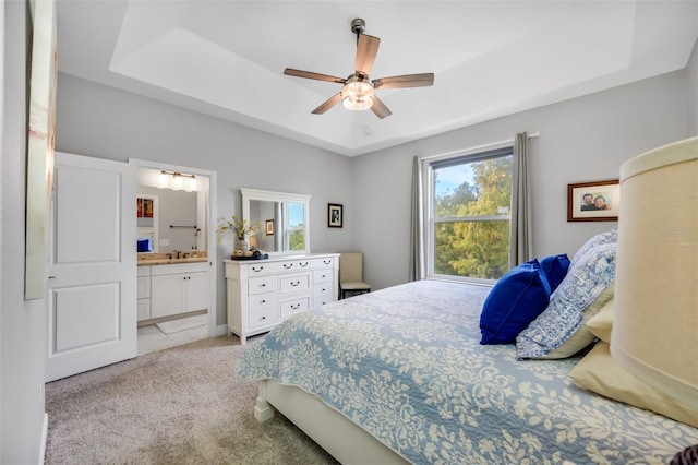 bedroom with ceiling fan, a raised ceiling, light colored carpet, and connected bathroom