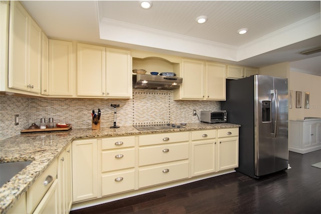 kitchen with stainless steel refrigerator with ice dispenser, black electric stovetop, extractor fan, a raised ceiling, and cream cabinetry