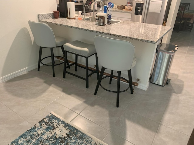 kitchen featuring light stone countertops, stainless steel fridge, a breakfast bar, and kitchen peninsula