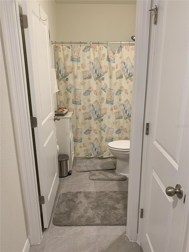 bathroom featuring toilet, curtained shower, and tile patterned flooring