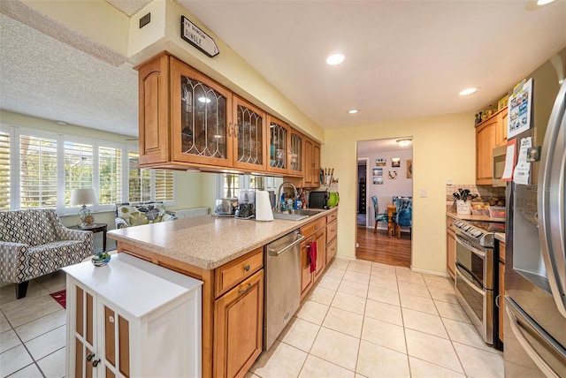 kitchen featuring sink, decorative backsplash, light tile patterned floors, a textured ceiling, and appliances with stainless steel finishes