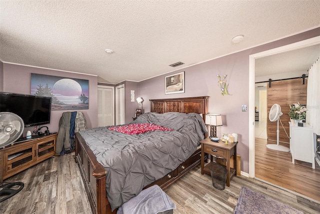 bedroom with hardwood / wood-style flooring, a barn door, a textured ceiling, and a closet