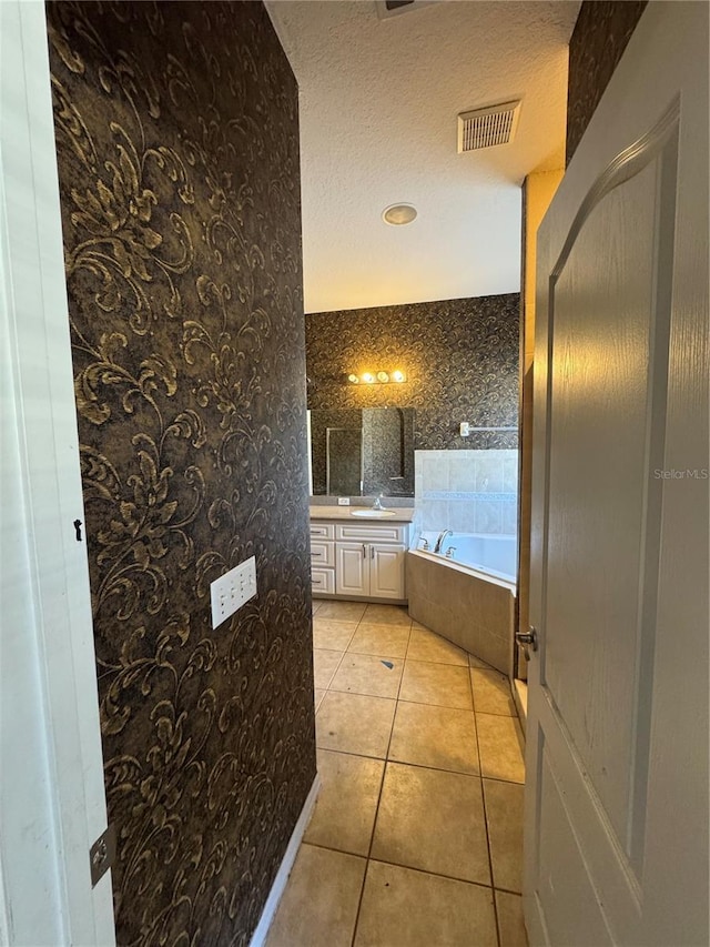 bathroom featuring tile patterned flooring, vanity, a textured ceiling, and a relaxing tiled tub