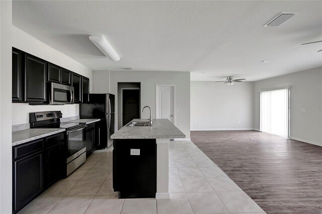 kitchen featuring sink, ceiling fan, an island with sink, appliances with stainless steel finishes, and light hardwood / wood-style floors