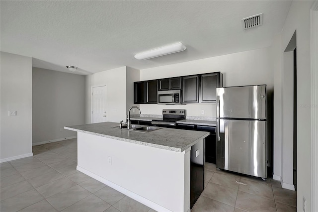 kitchen featuring appliances with stainless steel finishes, a textured ceiling, a kitchen island with sink, sink, and light tile patterned floors