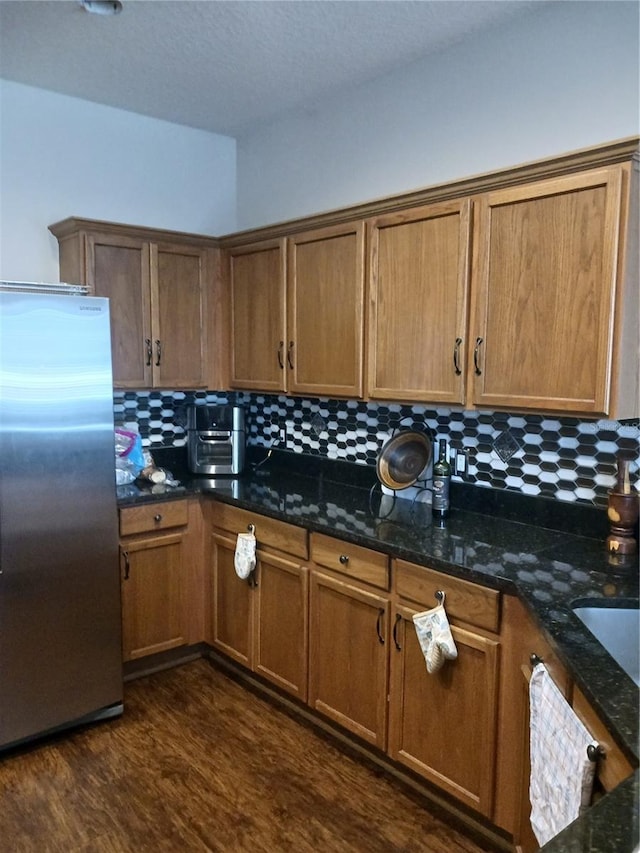 kitchen with decorative backsplash, stainless steel fridge, dark stone countertops, and dark hardwood / wood-style floors