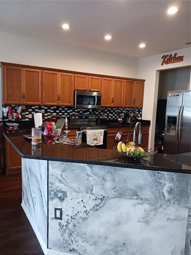 kitchen featuring dark wood-type flooring, appliances with stainless steel finishes, and dark stone countertops