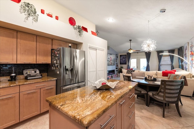 kitchen featuring light stone countertops, a kitchen island, stainless steel fridge, and backsplash