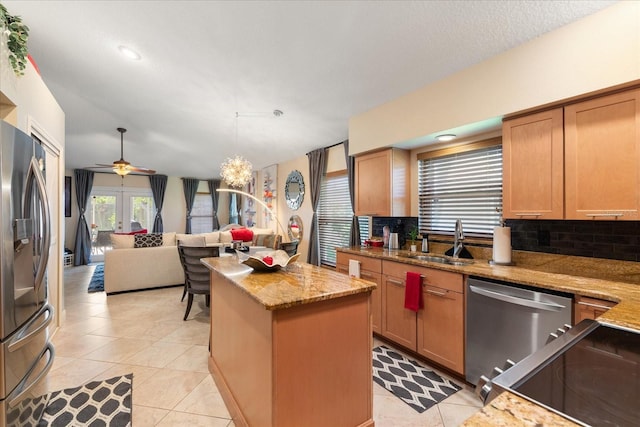 kitchen featuring sink, appliances with stainless steel finishes, light stone countertops, a kitchen island, and decorative backsplash