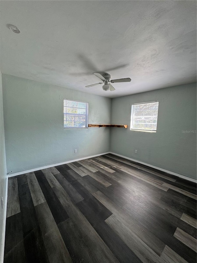 empty room featuring ceiling fan, plenty of natural light, and dark hardwood / wood-style flooring