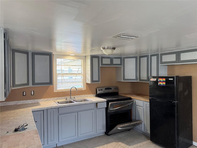 kitchen featuring sink, black fridge, light tile patterned floors, range with electric stovetop, and gray cabinets