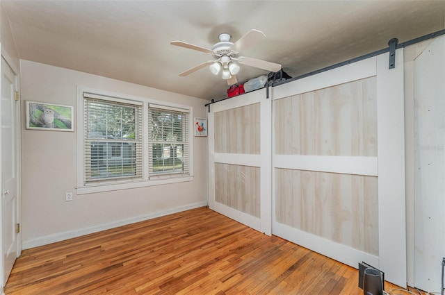 spare room featuring a barn door, hardwood / wood-style flooring, and ceiling fan