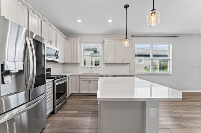 kitchen featuring stainless steel appliances, sink, pendant lighting, white cabinets, and a kitchen island