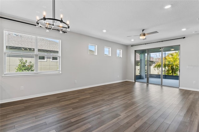 spare room with plenty of natural light, ceiling fan with notable chandelier, and dark hardwood / wood-style floors