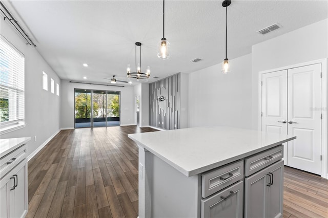 kitchen featuring ceiling fan with notable chandelier, decorative light fixtures, a kitchen island, and dark hardwood / wood-style floors