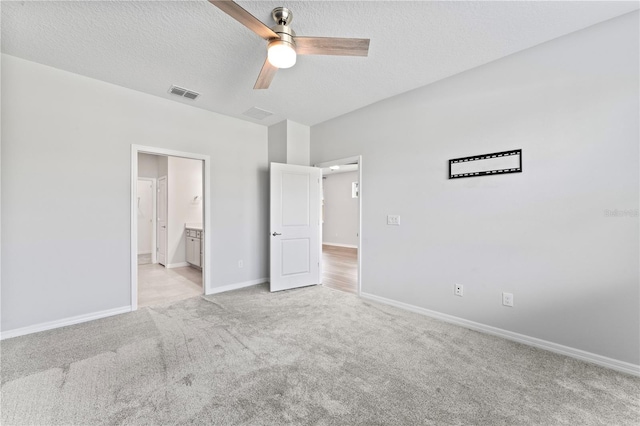 unfurnished bedroom featuring light carpet, a textured ceiling, ensuite bathroom, and ceiling fan