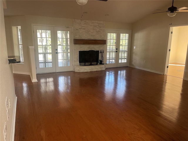 unfurnished living room with ceiling fan, a stone fireplace, a wealth of natural light, and french doors