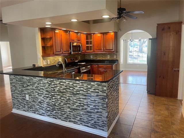 kitchen with tile patterned floors, kitchen peninsula, backsplash, ceiling fan with notable chandelier, and appliances with stainless steel finishes