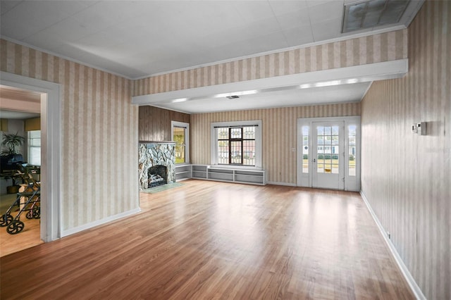 unfurnished living room with wood-type flooring, ornamental molding, and a stone fireplace