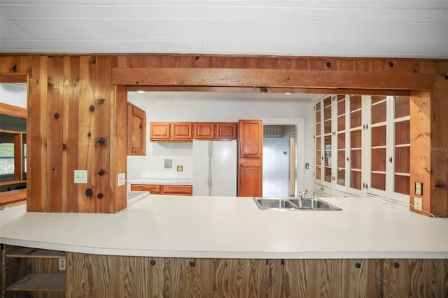 kitchen with sink, white refrigerator, wood walls, and kitchen peninsula